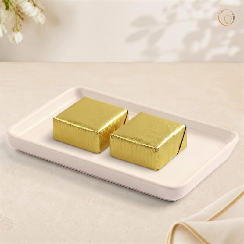 Chana Barfi - tabletop 2026 Radhe Chana Barfi, two pieces wrapped in gold foil on a white tray