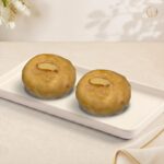 Radhe Galefa, two glazed ghee wheat discs topped with an almond sliver on a white tray